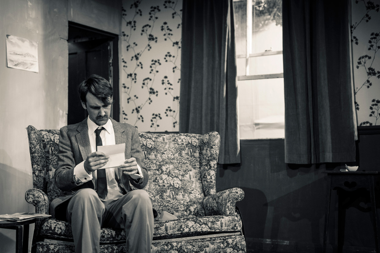 Man sitting on flowery sofa, reading a letter.